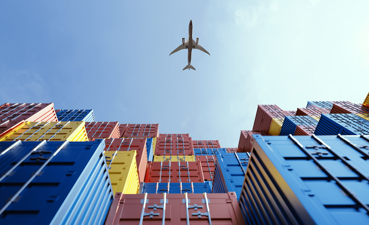 Stacked shipping containers beneath flying airplane